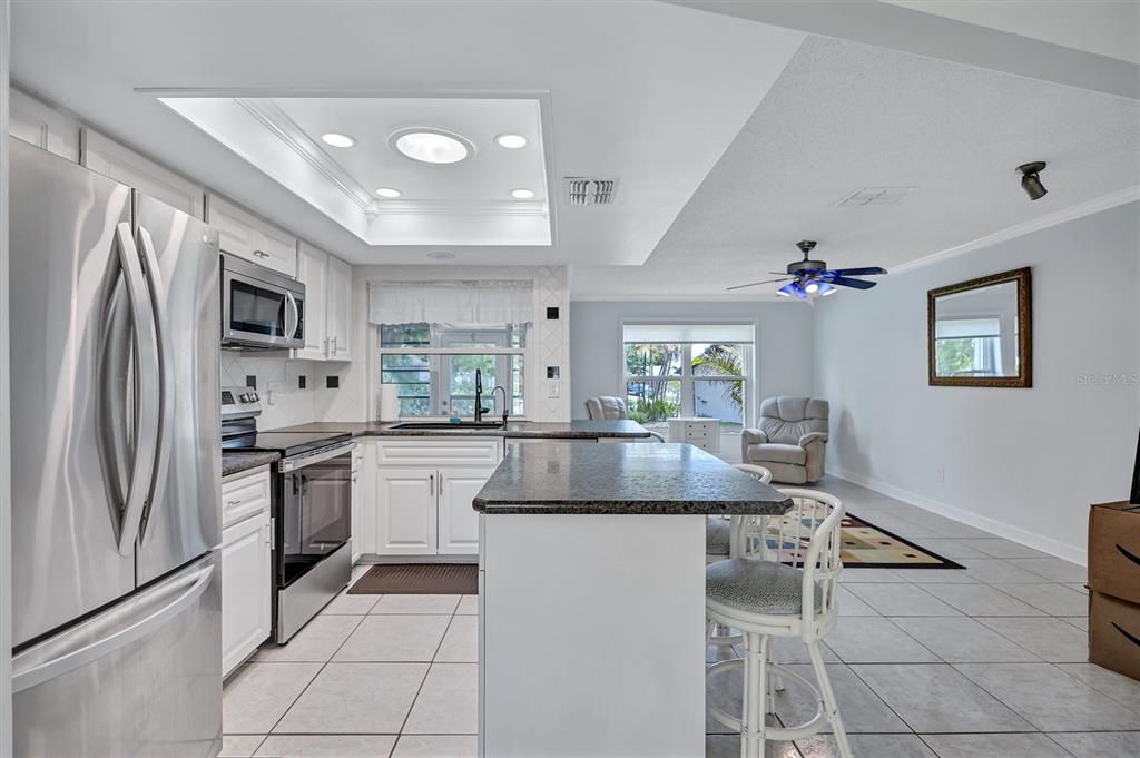 A kitchen with white cabinets, stainless steel appliances, and an island opens to a living area — 1735 ABERDEEN COURT, PALM HARBOR, FL