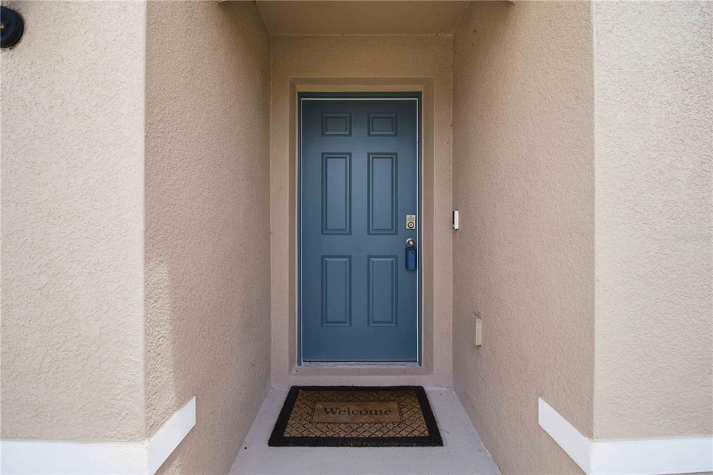 A blue front door with a welcome mat sits in a recessed entryway — 3906 111TH STREET E, PALMETTO, FL