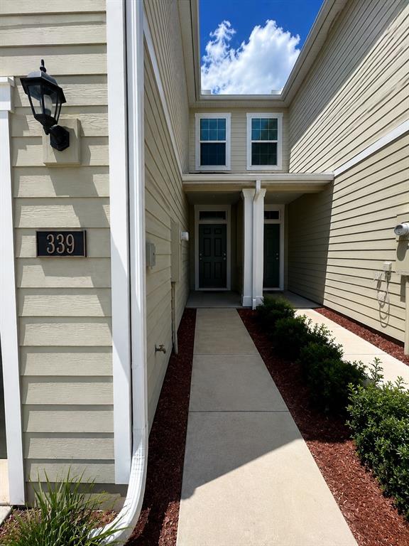 A concrete walkway leads to the recessed front entrances of a light-colored siding townhouse — 339 REDBUD ROAD, PALM COAST, FL