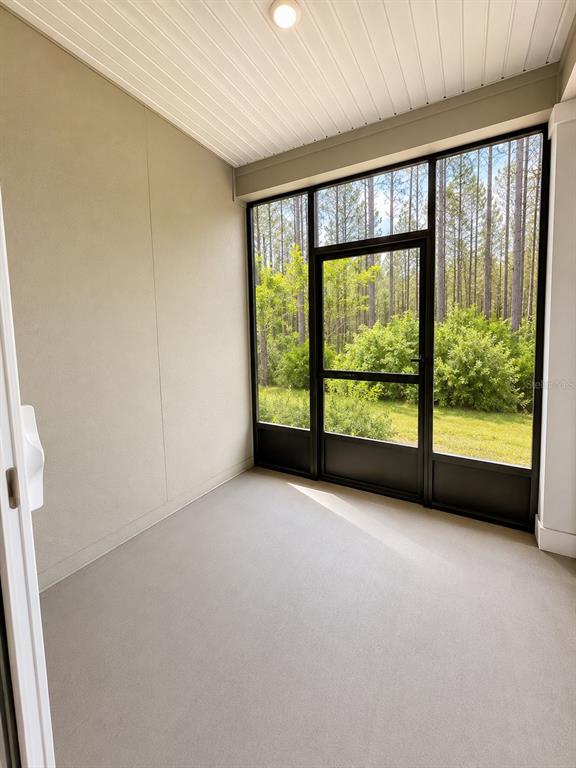 A screened-in porch with light-colored walls, a concrete floor, and a view of trees — 339 REDBUD ROAD, PALM COAST, FL