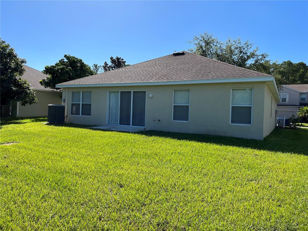 The rear exterior of a beige single-story house with a lawn and sliding glass doors — 5909 SWEET WILLIAM TERRACE, LAND O LAKES, FL