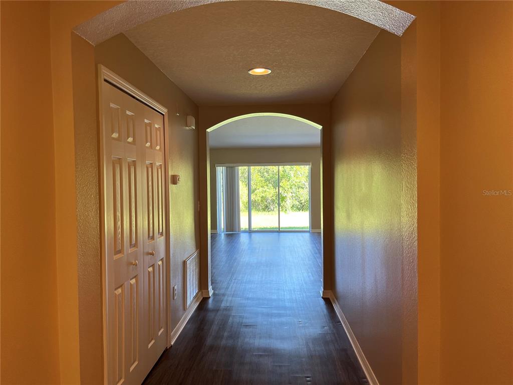 A hallway with dark wood-look flooring leads to an open living area with sliding doors — 5909 SWEET WILLIAM TERRACE, LAND O LAKES, FL