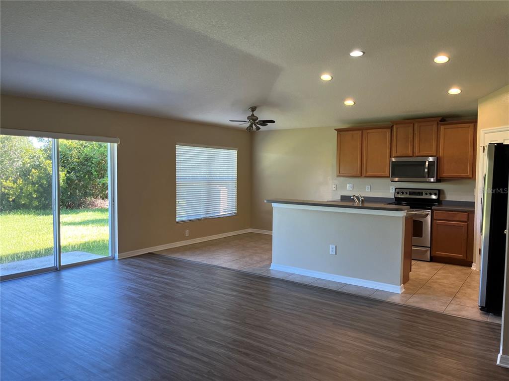An open-concept living area features wood-look flooring, a kitchen with wood cabinets, and sliding doors — 5909 SWEET WILLIAM TERRACE, LAND O LAKES, FL