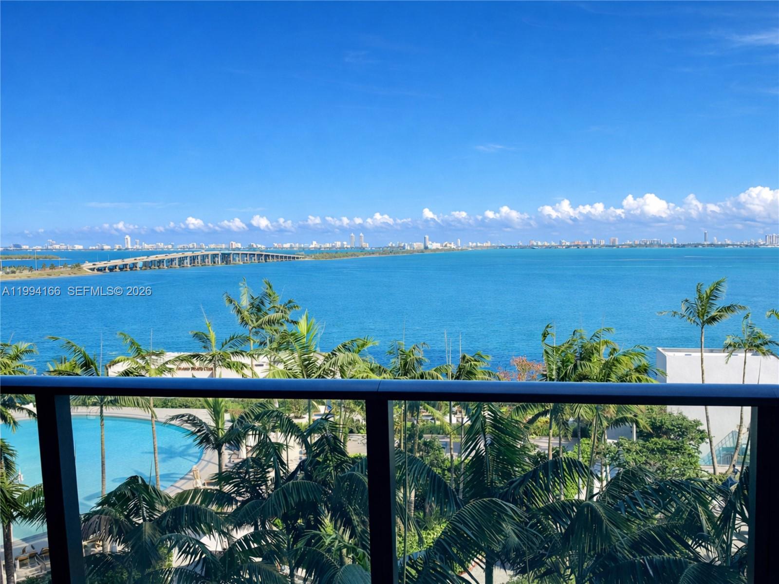 A balcony view overlooks a swimming pool, palm trees, a bridge, and the ocean — 480 NE 31st St # 802, Miami FL 33137, MIAMI, FL