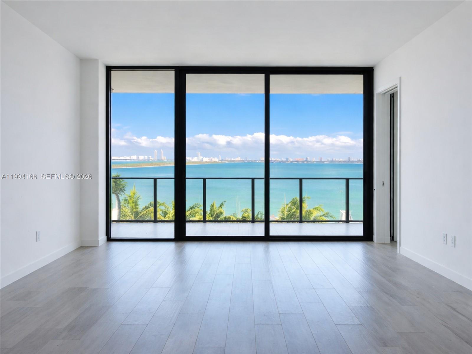 An empty room with light wood floors and floor-to-ceiling windows overlooking the ocean — 480 NE 31st St # 802, Miami FL 33137, MIAMI, FL
