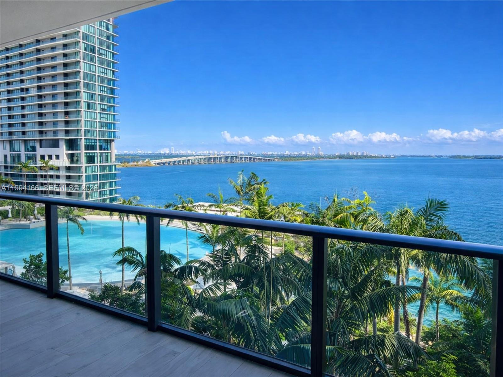 A balcony overlooks a swimming pool, palm trees, a bridge, and the ocean — 480 NE 31st St # 802, Miami FL 33137, MIAMI, FL