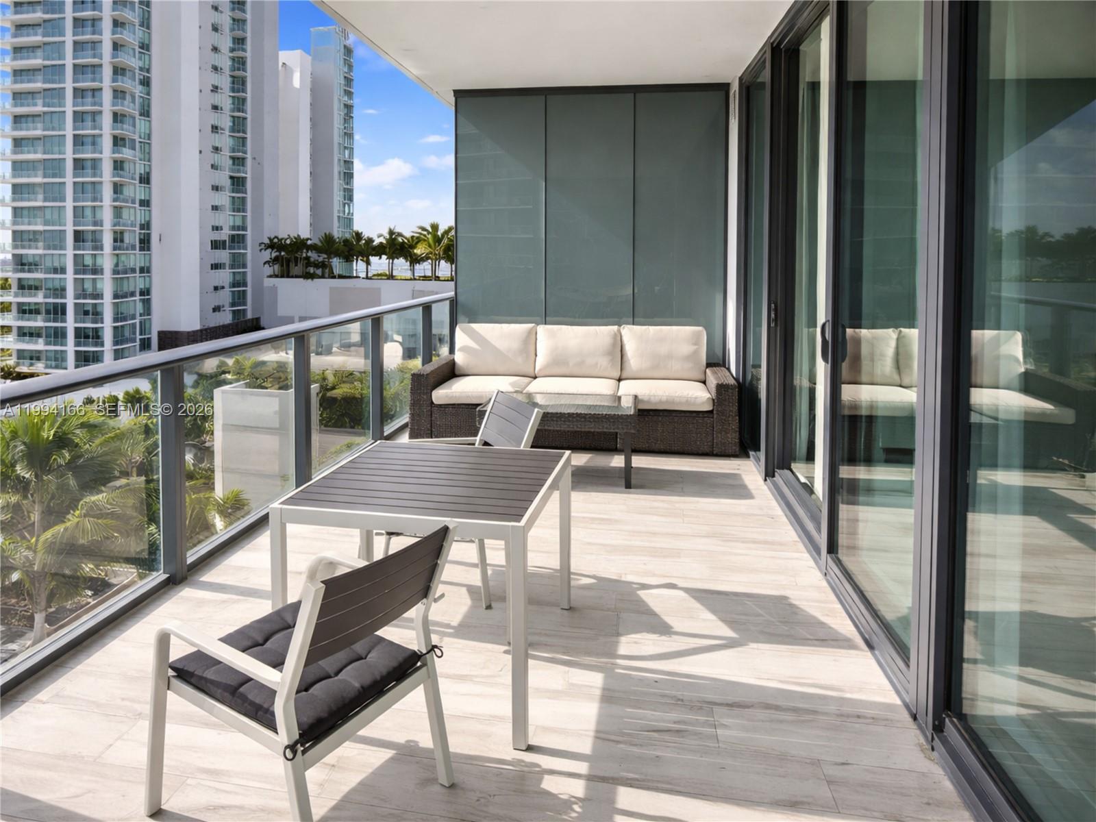 A balcony with outdoor furniture, light wood-look tile flooring, and a glass railing overlooking buildings — 480 NE 31st St # 802, Miami FL 33137, MIAMI, FL
