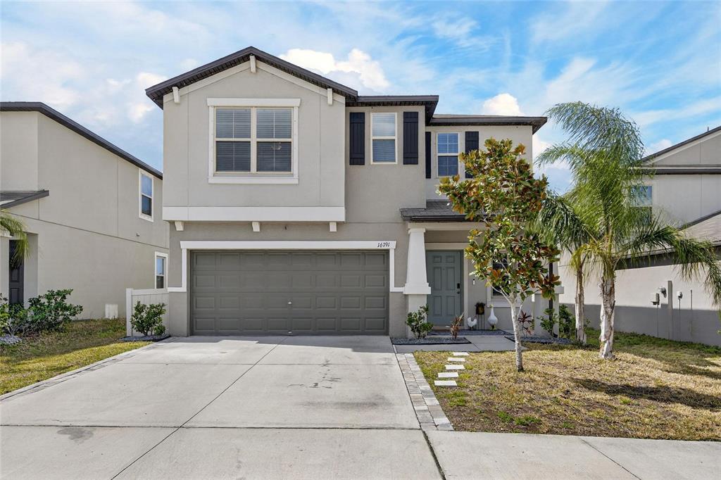 The exterior of a house features a light blue front door, a covered porch, and landscaping — 16791 DELIA STREET, WIMAUMA, FL