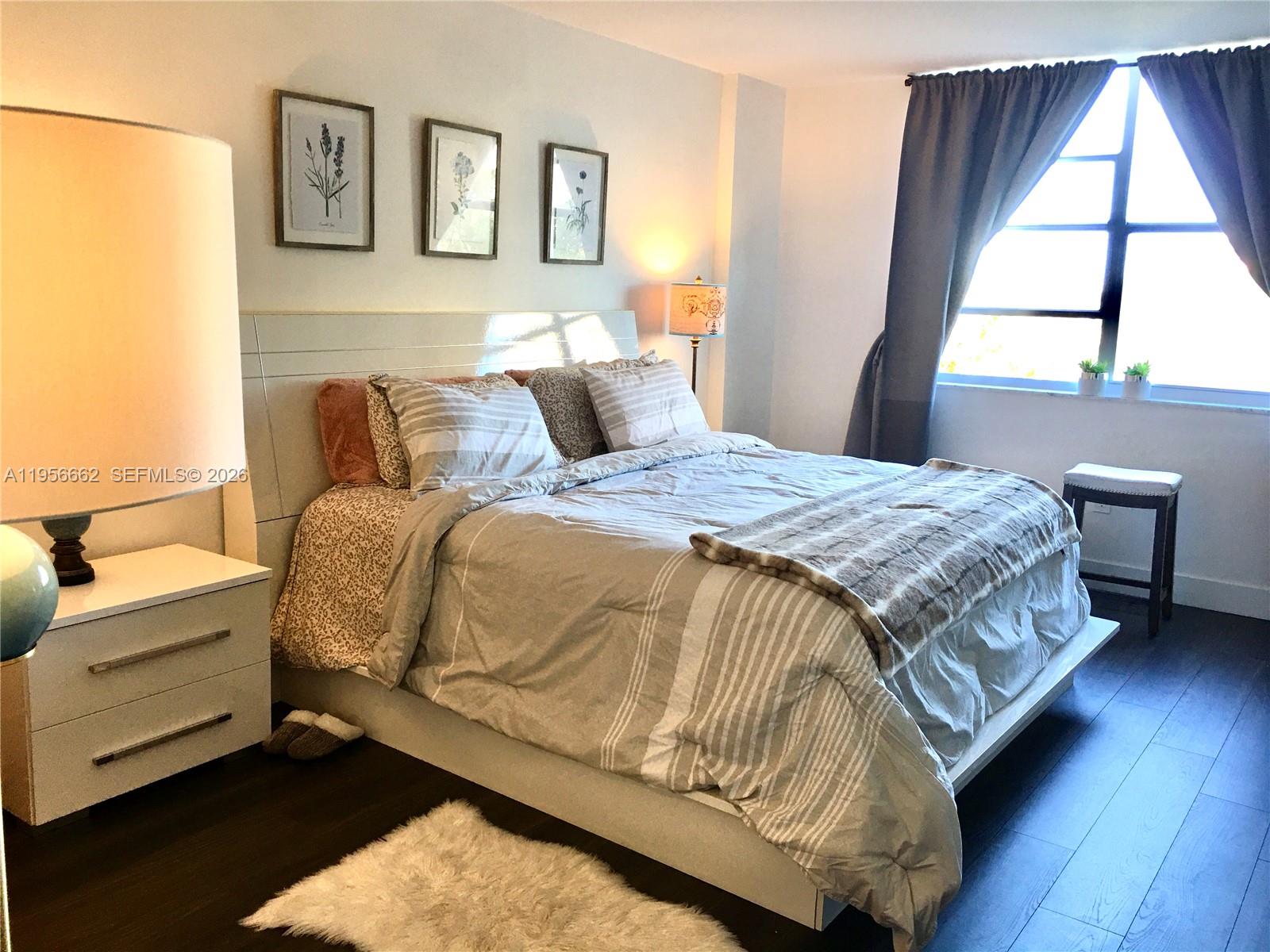 A bedroom features a bed with striped bedding, a white nightstand, and a window with curtains — 11111 Biscayne Blvd # 4D, Miami FL 33181, MIAMI, FL