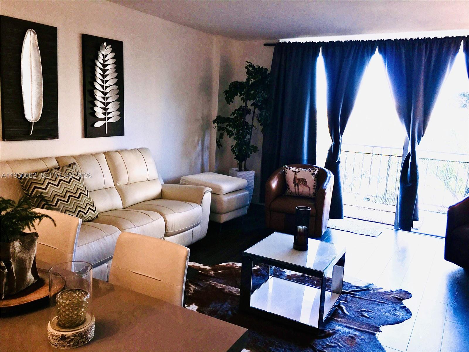 A living room features a cream sofa, leather armchair, cowhide rug, and dark curtains — 11111 Biscayne Blvd # 4D, Miami FL 33181, MIAMI, FL