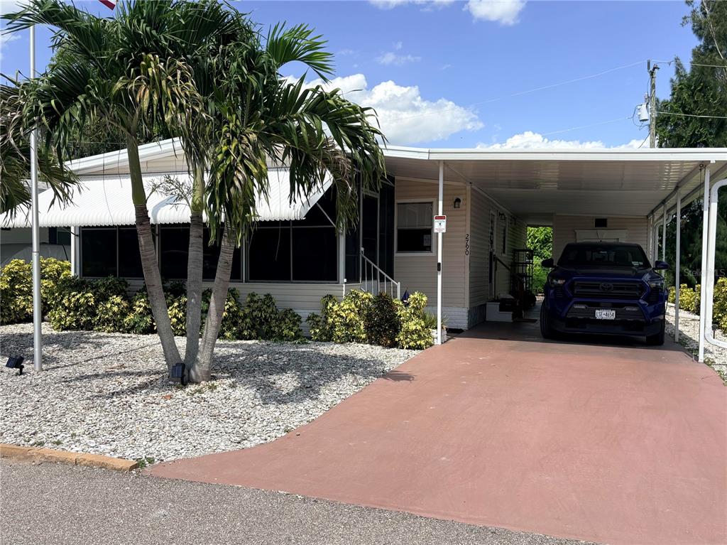 A single-story mobile home with a screened-in porch, carport, and a blue truck parked outside — 2790 INDIANWOOD DRIVE, NORTH FORT MYERS, FL