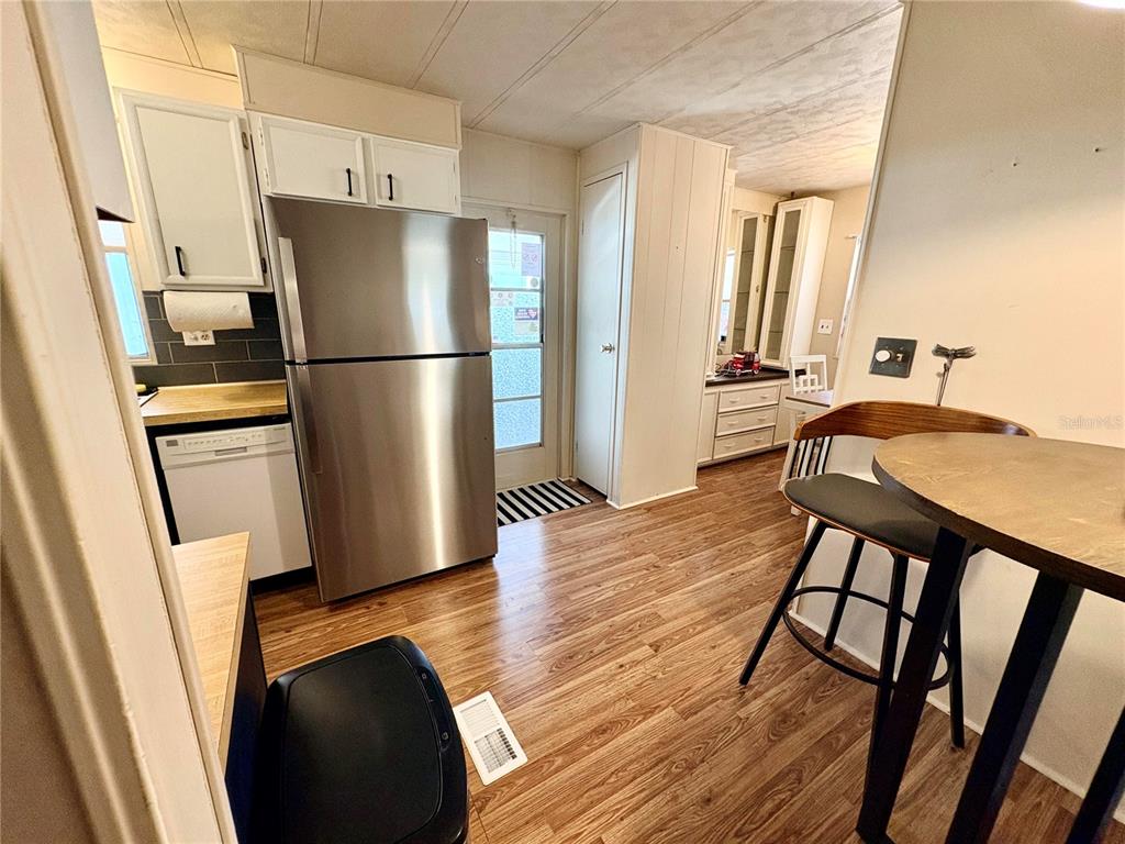 A kitchen features stainless steel appliances, white cabinetry, wood-look flooring, and a small dining area — 2790 INDIANWOOD DRIVE, NORTH FORT MYERS, FL