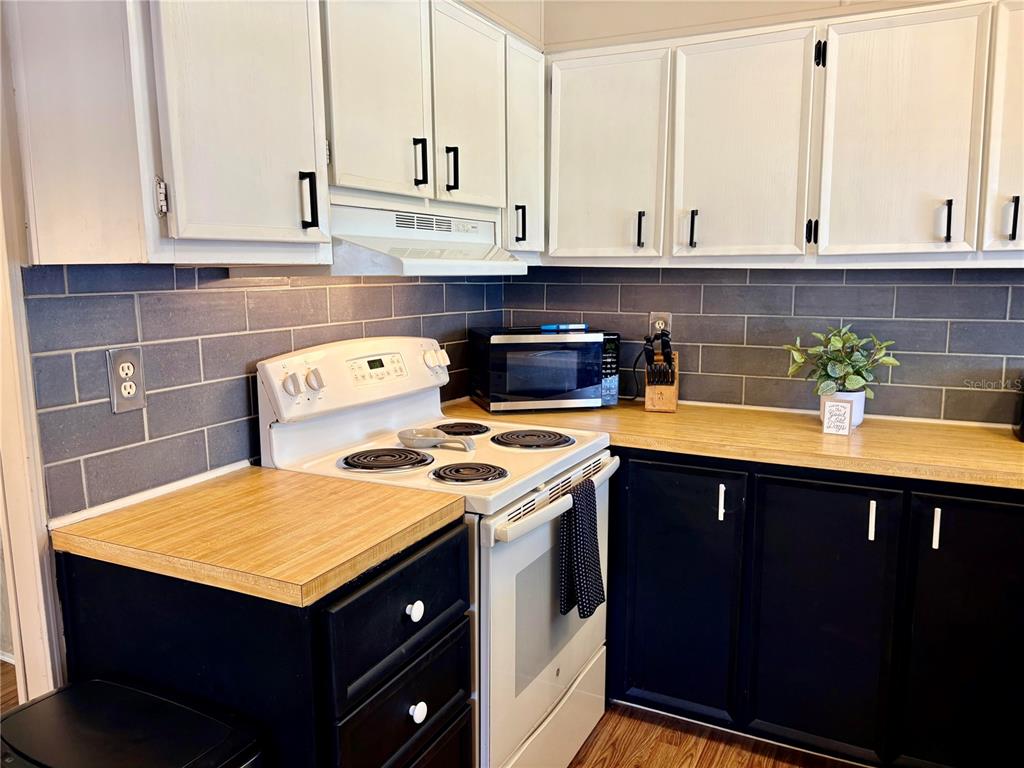 A kitchen features white upper cabinets, dark lower cabinets, wood countertops, and a gray backsplash — 2790 INDIANWOOD DRIVE, NORTH FORT MYERS, FL