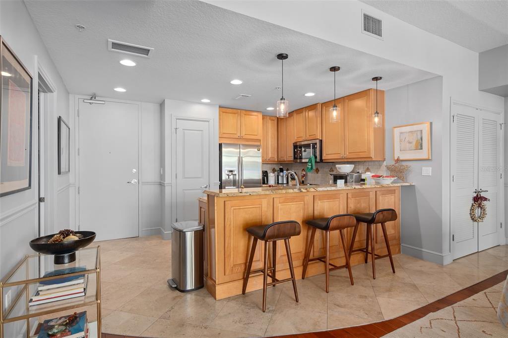 A kitchen features light wood cabinets, granite countertops, a breakfast bar with stools, and tile flooring — 101 S EOLA DRIVE UNIT 1209, ORLANDO, FL