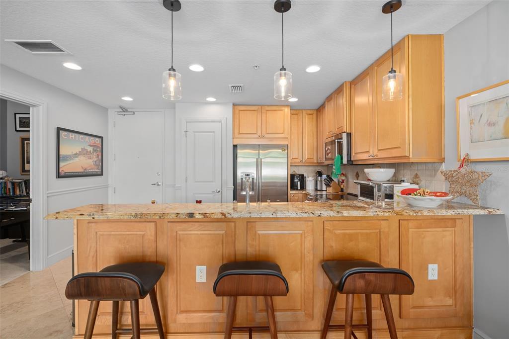 A kitchen features light wood cabinets, granite countertops, three bar stools, and pendant lighting — 101 S EOLA DRIVE UNIT 1209, ORLANDO, FL