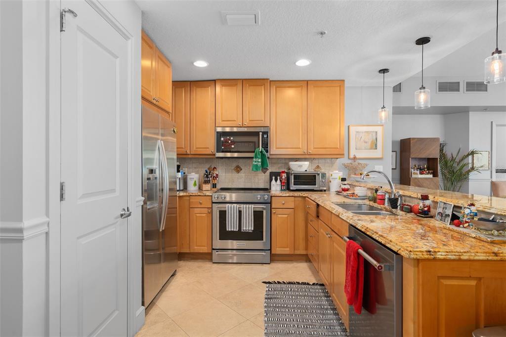 A kitchen features light wood cabinets, granite countertops, stainless steel appliances, and tile flooring — 101 S EOLA DRIVE UNIT 1209, ORLANDO, FL
