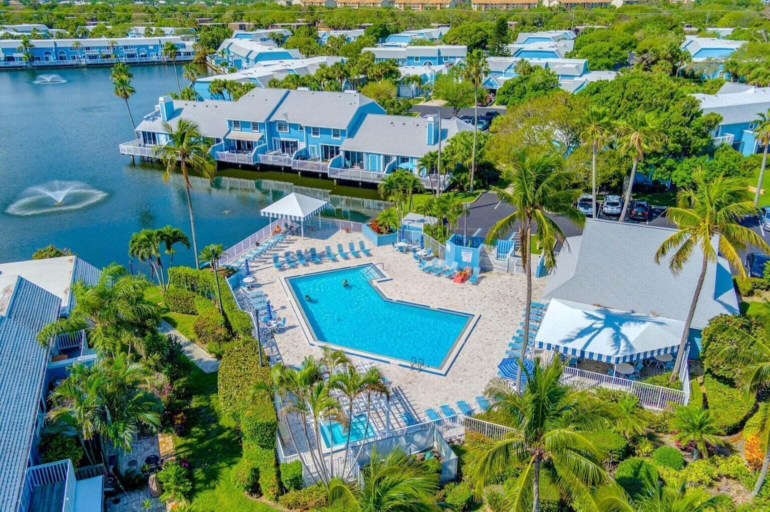 An aerial view of a swimming pool and clubhouse surrounded by blue waterfront townhomes — 716 Ocean Dunes Circle, Jupiter FL 33477, JUPITER, FL