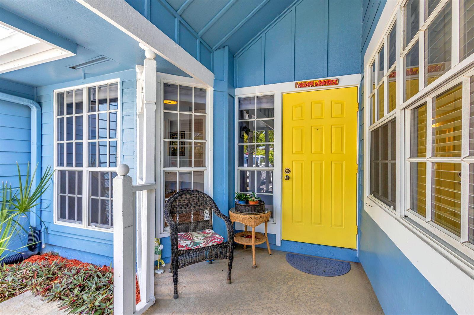 A bright yellow front door sits on a blue porch with a wicker chair — 716 Ocean Dunes Circle, Jupiter FL 33477, JUPITER, FL