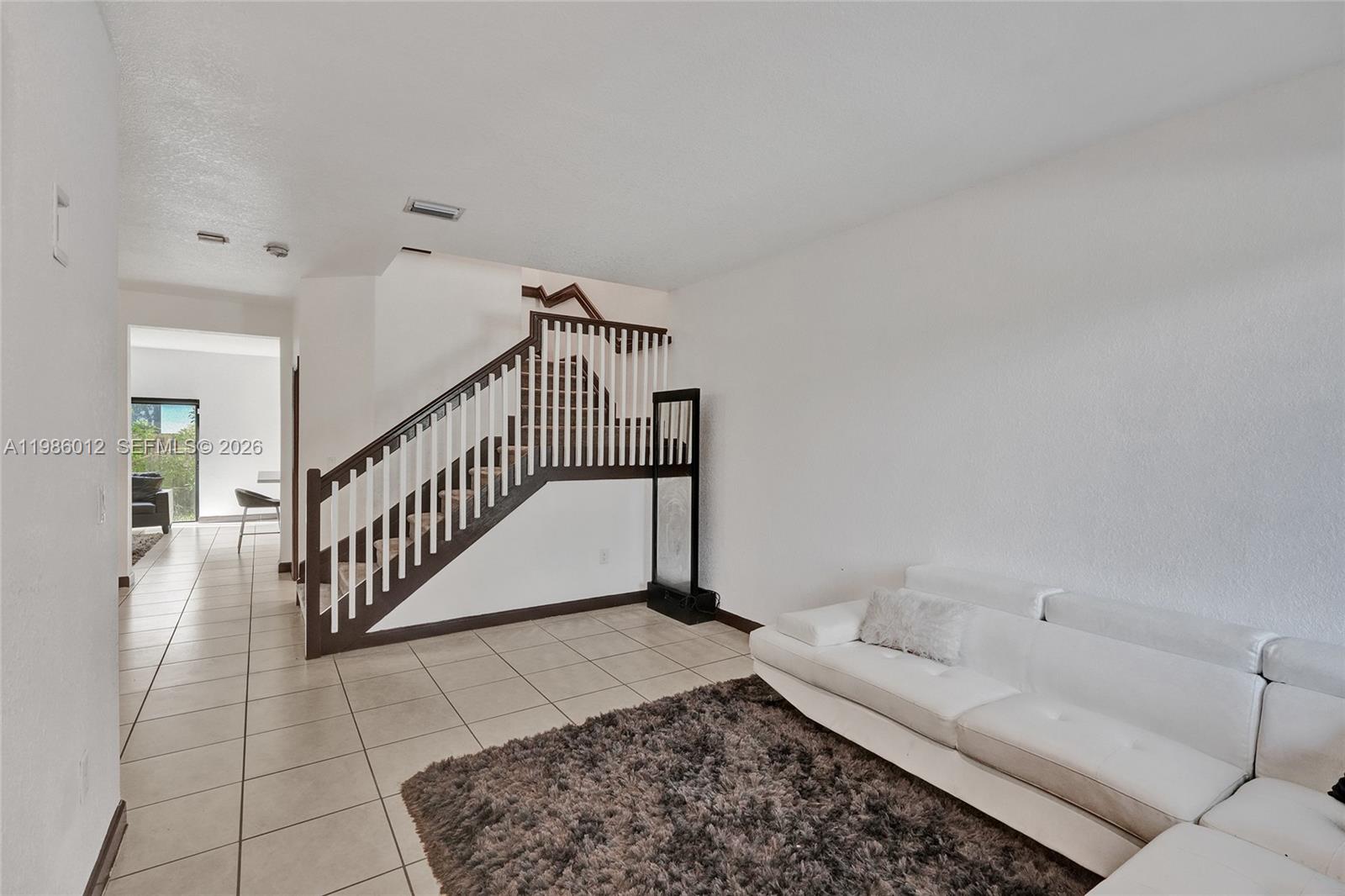 A living room features a white sofa, a shaggy rug, and a wooden staircase — 408 NE 212th Ter, Miami FL 33179, MIAMI, FL
