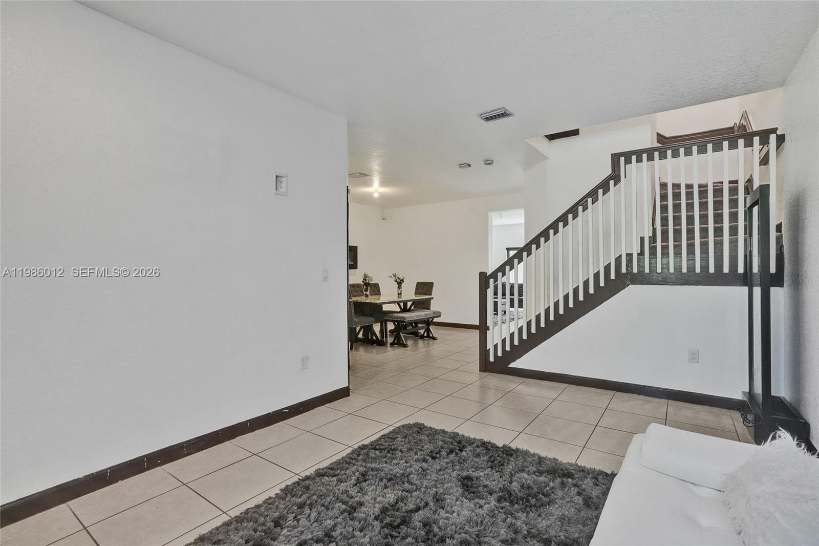 A living area with tile flooring leads to a dining space and a wooden staircase — 408 NE 212th Ter, Miami FL 33179, MIAMI, FL
