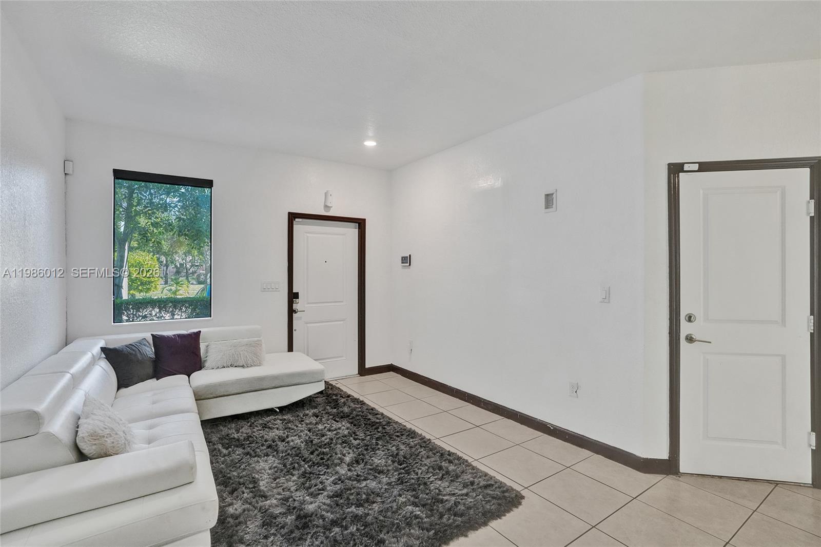 A living room features white walls, tile flooring, a white sectional sofa, and two doors — 408 NE 212th Ter, Miami FL 33179, MIAMI, FL