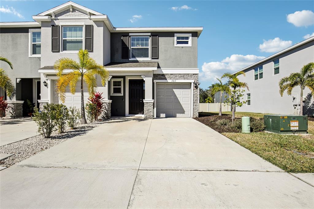 A two-story townhouse features a gray stucco facade, stone accents, and a single-car garage — 2813 MIDNIGHT PEARL DRIVE, SARASOTA, FL