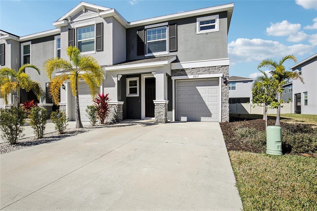 A two-story townhouse with a gray stucco facade, stone accents, and a single-car garage — 2813 MIDNIGHT PEARL DRIVE, SARASOTA, FL