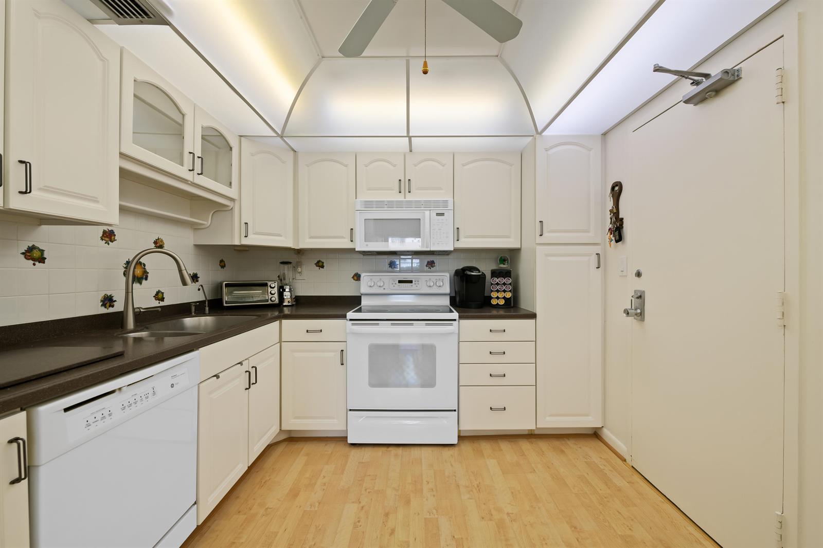 A kitchen with white cabinets, dark countertops, a white stove, and light wood flooring — 10777 W Sample # 207, Coral Springs FL 33065, CORAL SPRINGS, FL