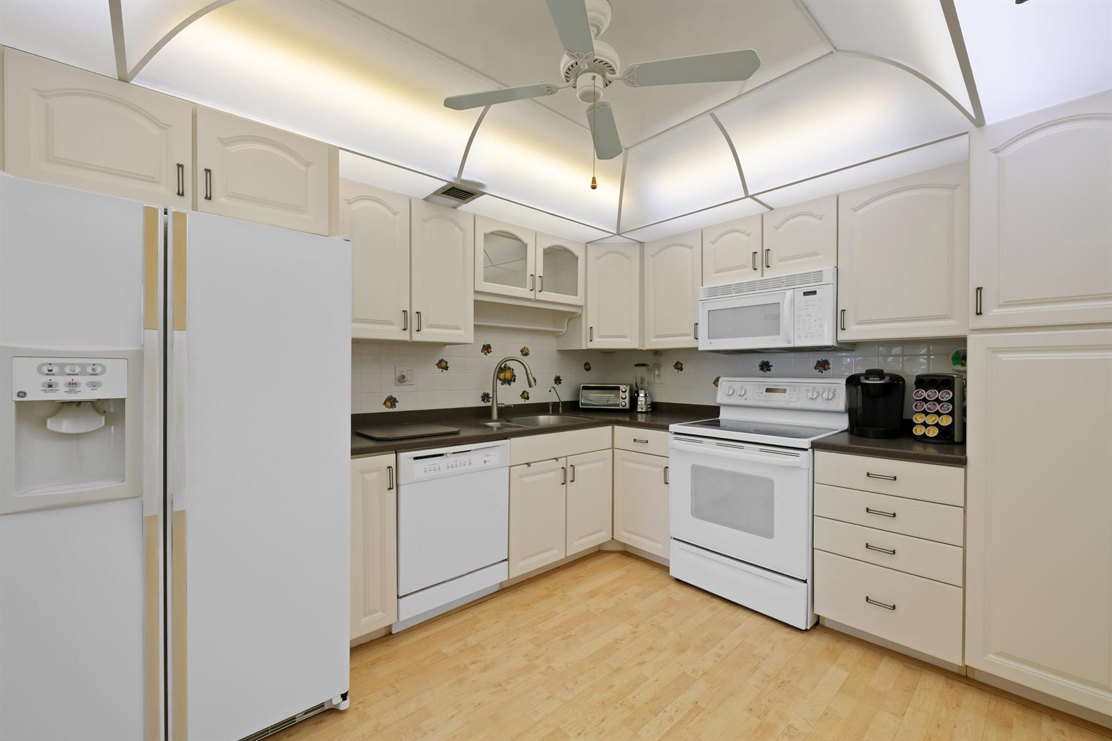 A kitchen with white appliances, light-colored cabinetry, and a ceiling fan under a tray ceiling — 10777 W Sample # 207, Coral Springs FL 33065, CORAL SPRINGS, FL
