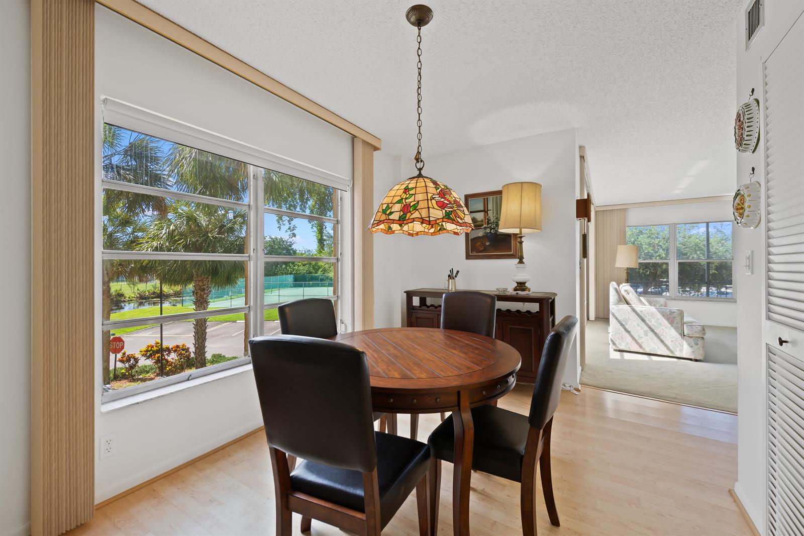 A dining area features a round wooden table, four chairs, and a stained-glass pendant light — 10777 W Sample # 207, Coral Springs FL 33065, CORAL SPRINGS, FL