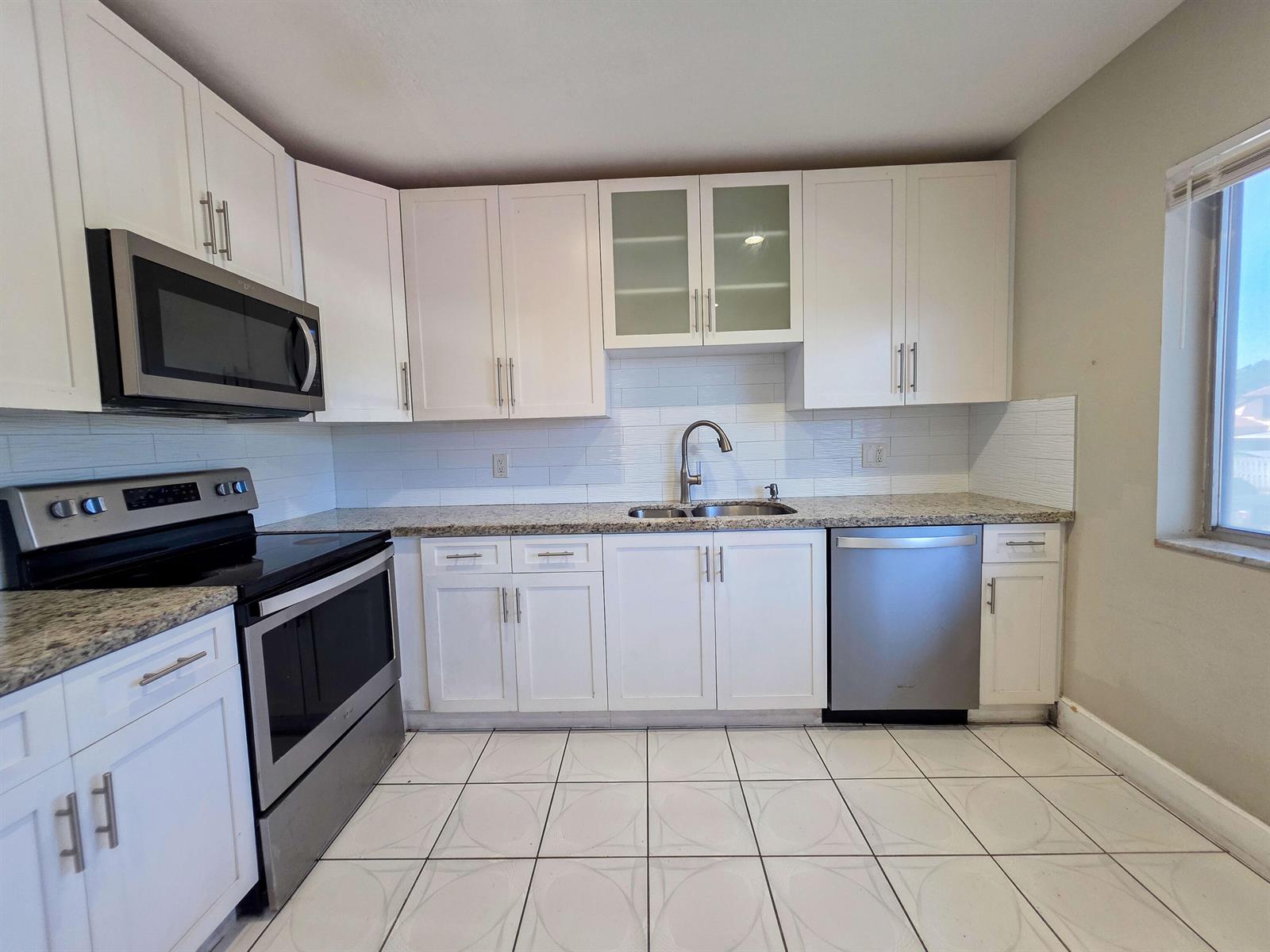 A kitchen features white cabinets, stainless steel appliances, granite countertops, and white tiled flooring — 6289 Lear Drive # 203, Lake Worth FL 33462, LAKE WORTH, FL