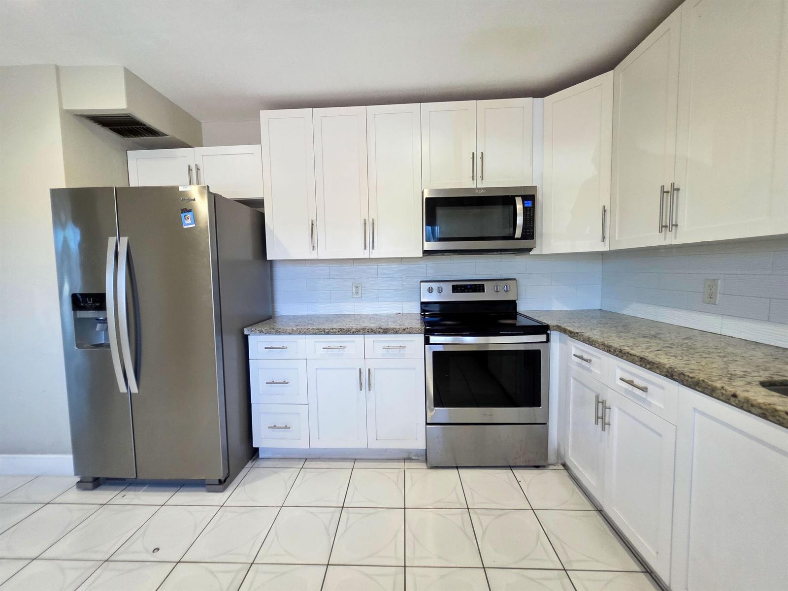 A kitchen with white cabinets, stainless steel appliances, granite countertops, and white tiled flooring — 6289 Lear Drive # 203, Lake Worth FL 33462, LAKE WORTH, FL