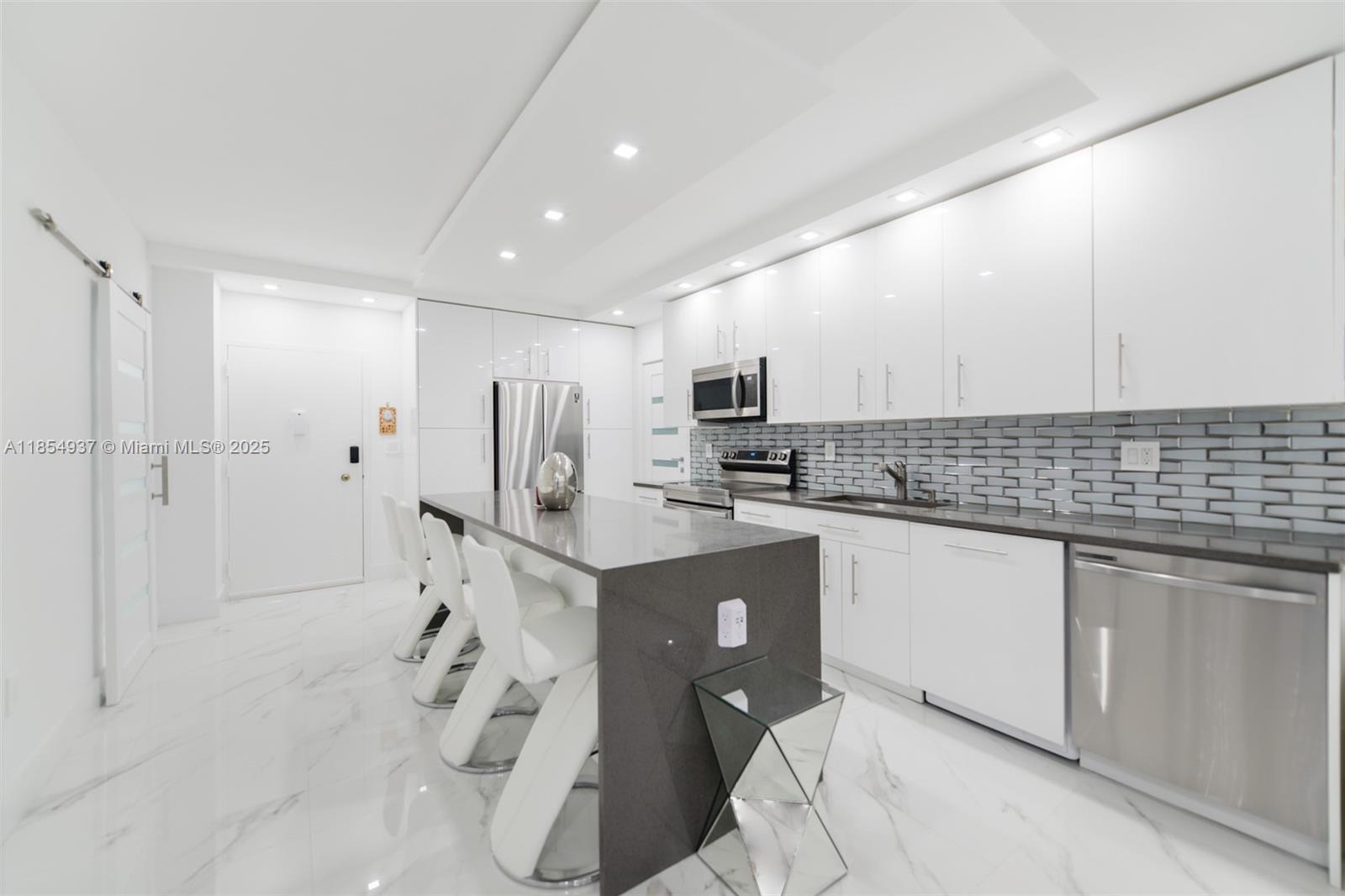 A modern kitchen features white cabinets, a dark gray island, and white marble-style flooring — 1980 S Ocean Dr, Hallandale Beach FL 33009, HALLANDALE BEACH, FL