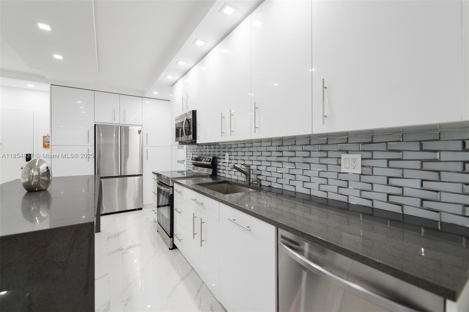 A modern kitchen features white cabinets, dark gray countertops, stainless steel appliances, and tile backsplash — 1980 S Ocean Dr, Hallandale Beach FL 33009, HALLANDALE BEACH, FL