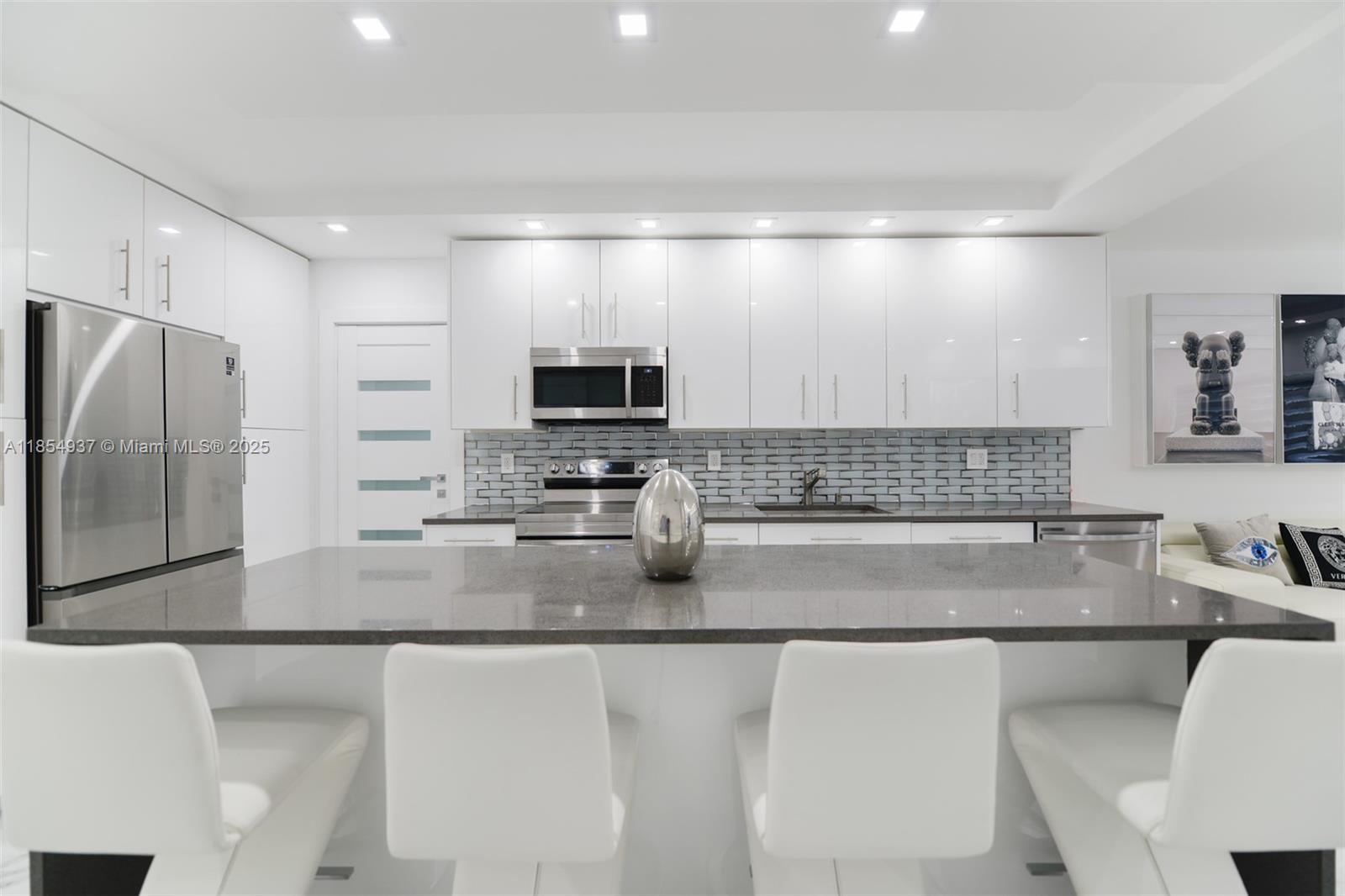 A modern kitchen features white cabinetry, a dark gray island, stainless steel appliances, and barstools — 1980 S Ocean Dr, Hallandale Beach FL 33009, HALLANDALE BEACH, FL