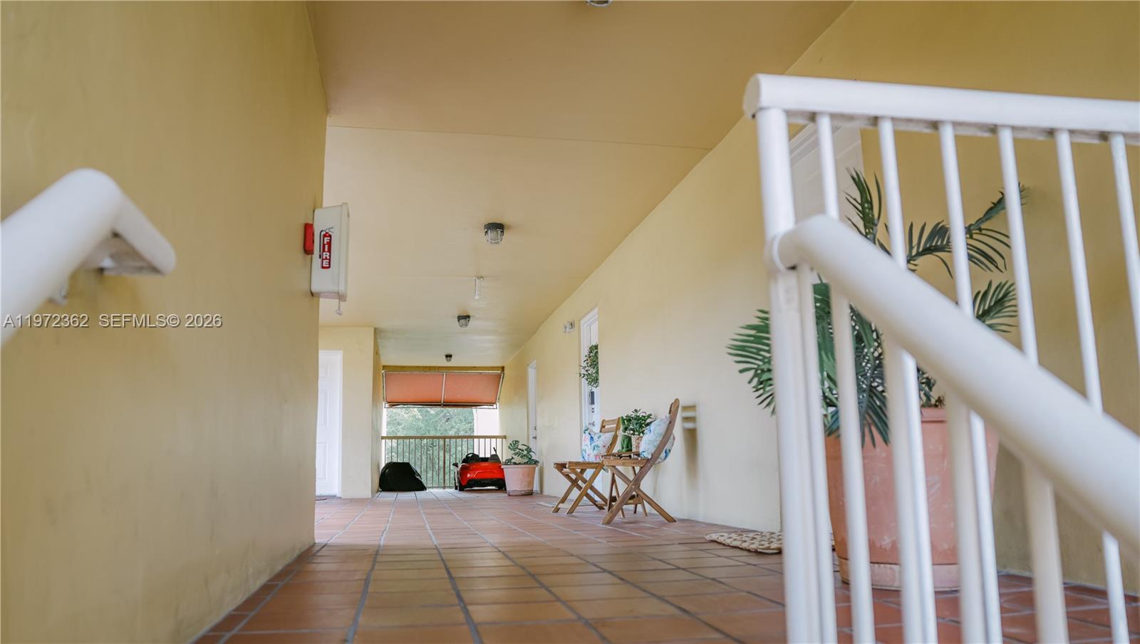 An outdoor tiled walkway features a white railing, wooden chairs, and a fire extinguisher — 13820 SW 112th St # 204, Miami FL 33186, MIAMI, FL