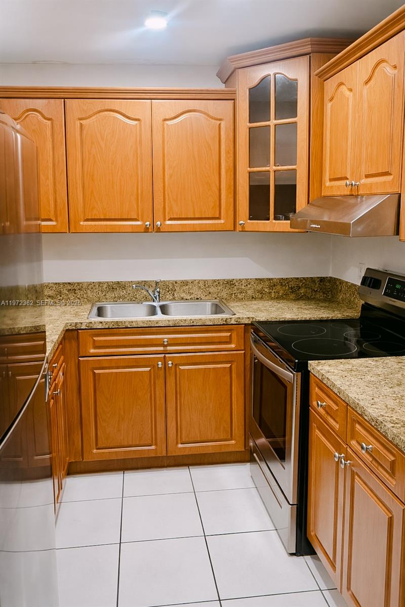A kitchen features wood cabinets, granite countertops, stainless steel appliances, and white tile flooring — 13820 SW 112th St # 204, Miami FL 33186, MIAMI, FL