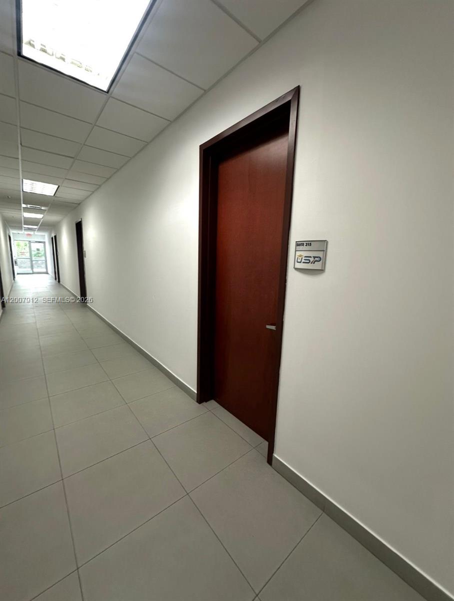 A hallway with light-colored tile flooring leads to a dark wood door labeled Suite 215 — 1500 NW 89th Ct # 217, Doral FL 33172, DORAL, FL