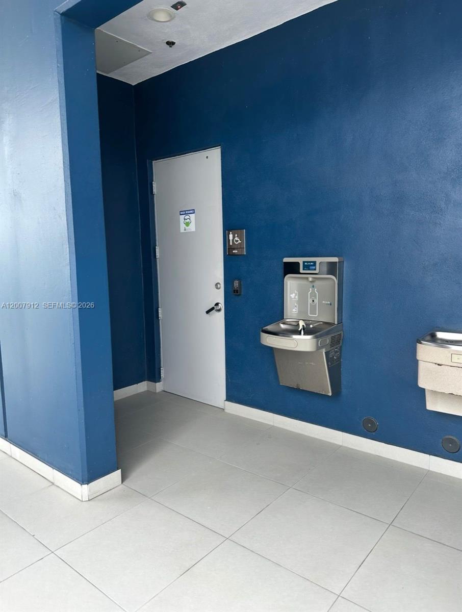 A blue-walled hallway features a white door, a water fountain, and tile flooring — 1500 NW 89th Ct # 217, Doral FL 33172, DORAL, FL