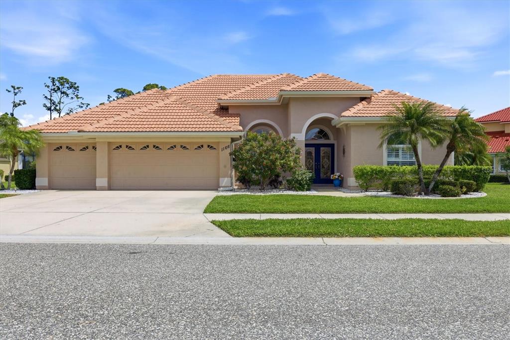 A single-story house with a tan stucco exterior, tile roof, and a three-car garage — 1166 EAGLES FLIGHT WAY, NORTH PORT, FL