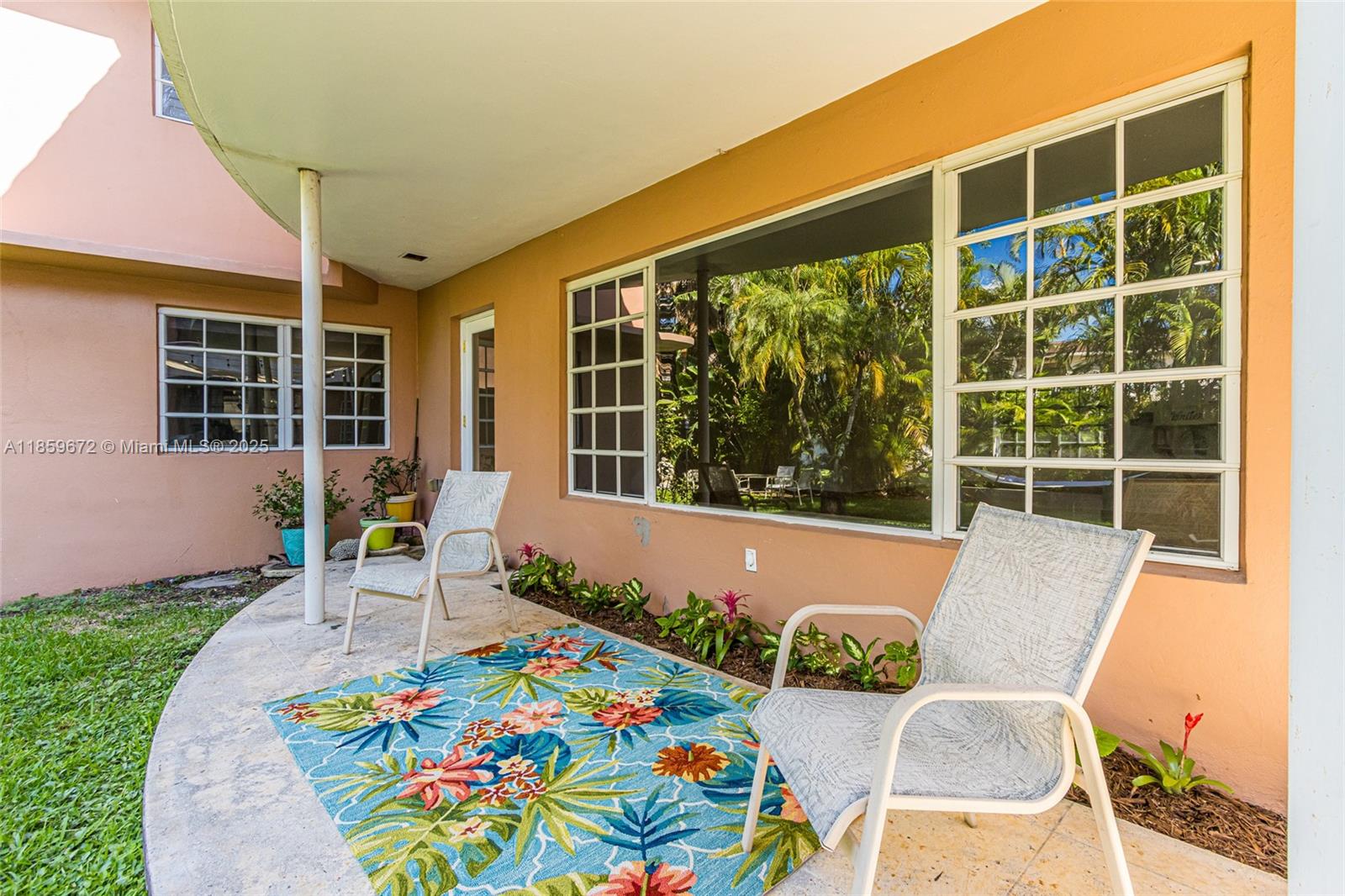 A covered patio features two chairs, a floral rug, and large windows on a peach-colored wall — 60 Park Dr # C, Bal Harbour FL 33154, BAL HARBOUR, FL