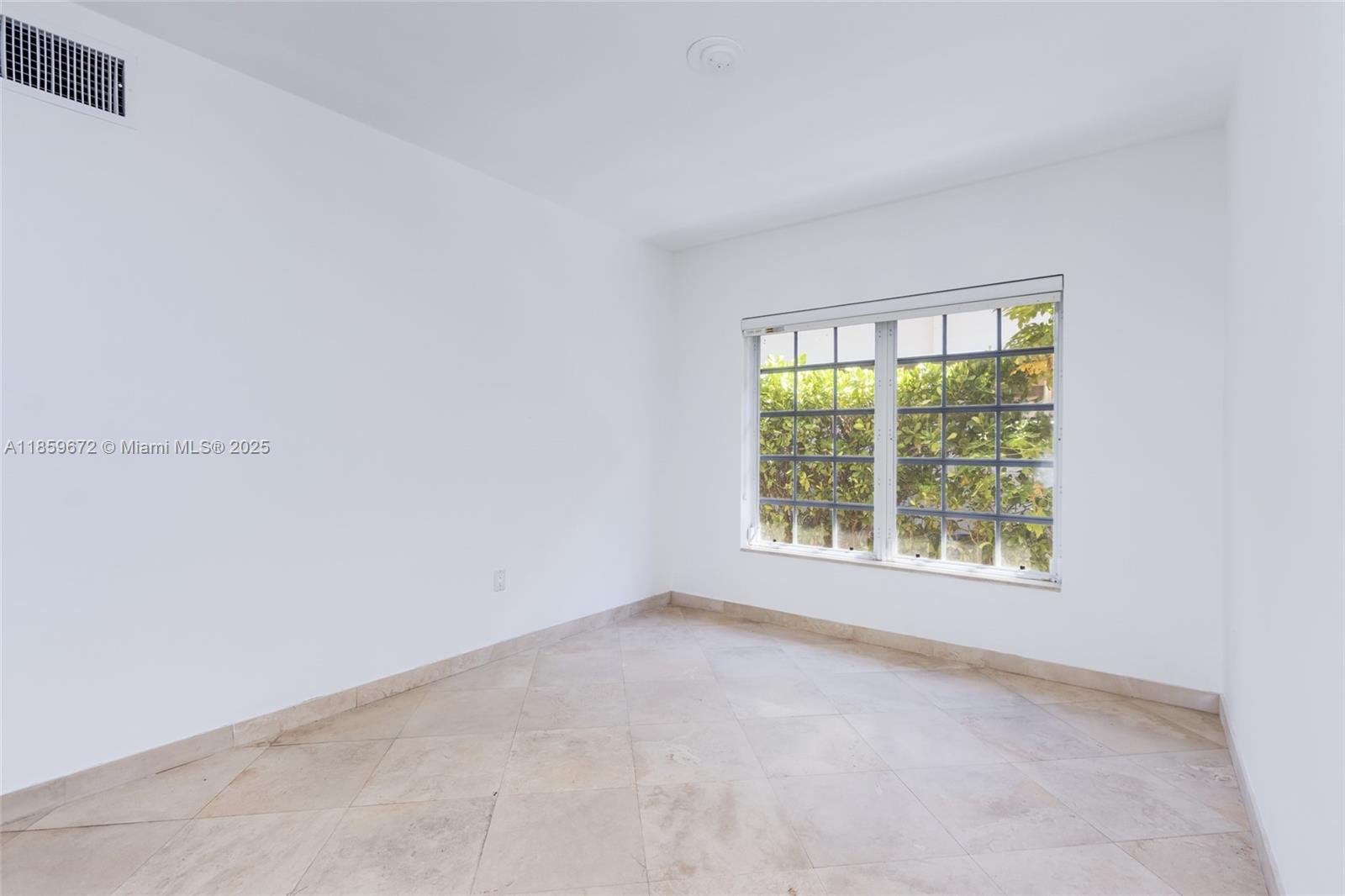 An empty room features white walls, light-colored tile flooring, and a large window with greenery — 60 Park Dr # C, Bal Harbour FL 33154, BAL HARBOUR, FL