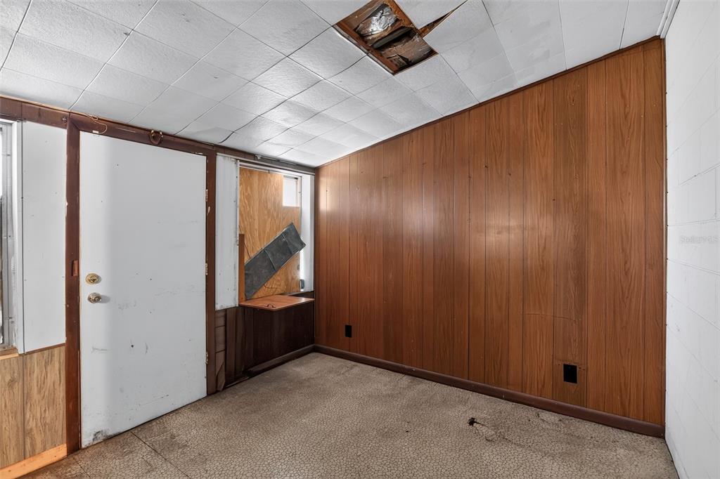 An interior room features wood-paneled walls, a damaged drop ceiling, and a carpeted floor — 6120 W RIDGEWOOD AVENUE, ORLANDO, FL