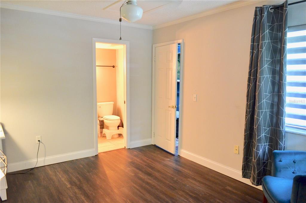 A bedroom with wood-look flooring, a ceiling fan, and an open doorway to a bathroom — 101 N HILL AVENUE UNIT 5, DELAND, FL