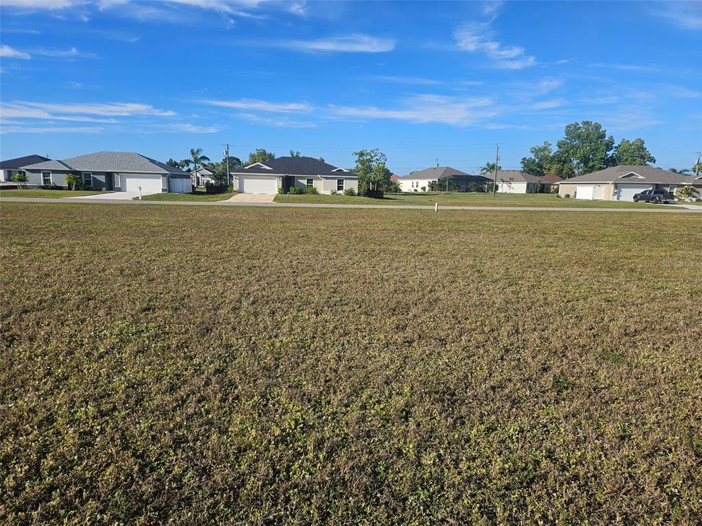 A large, flat, grassy vacant lot sits in front of several suburban houses — 25241 CADIZ DRIVE, PUNTA GORDA, FL