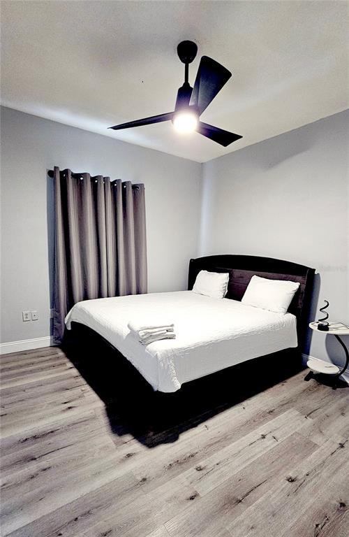 A bedroom features a dark bed frame, light wood-look flooring, and a ceiling fan — 13612 N 21ST STREET UNIT 2, TAMPA, FL