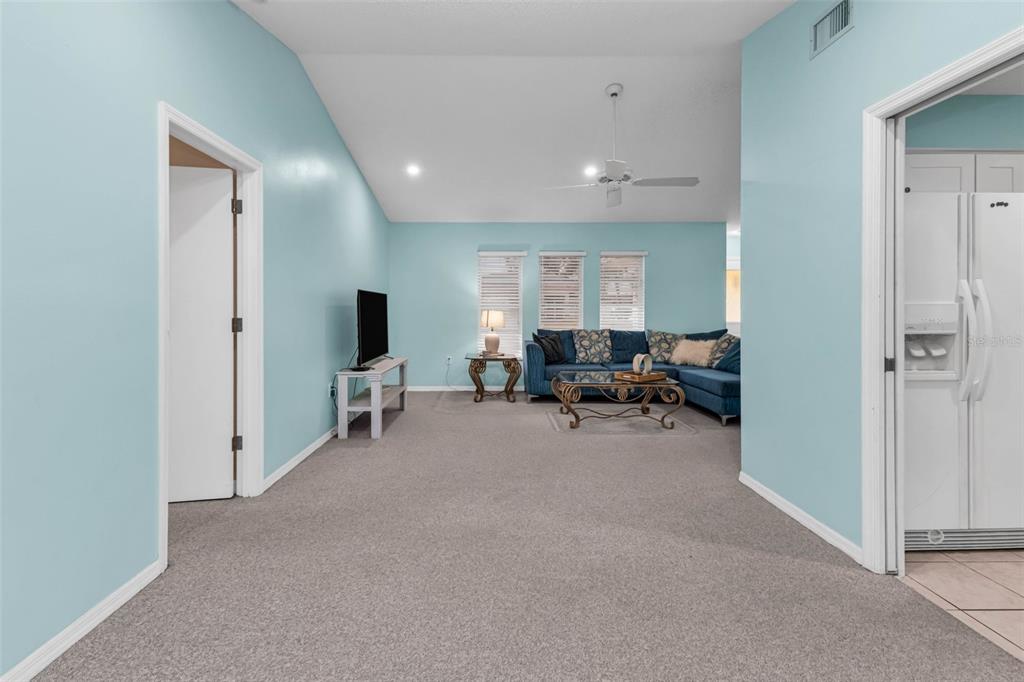 A living room with light blue walls, vaulted ceilings, gray carpeting, and a blue sectional sofa — 285 MARK TWAIN LANE, ROTONDA WEST, FL