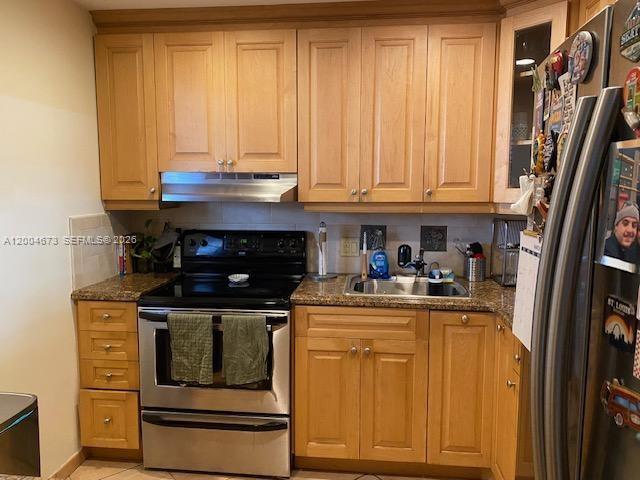 A kitchen features light wood cabinets, stainless steel appliances, and tan tile flooring — 100 Edgewater Dr # 102, Coral Gables FL 33133, CORAL GABLES, FL