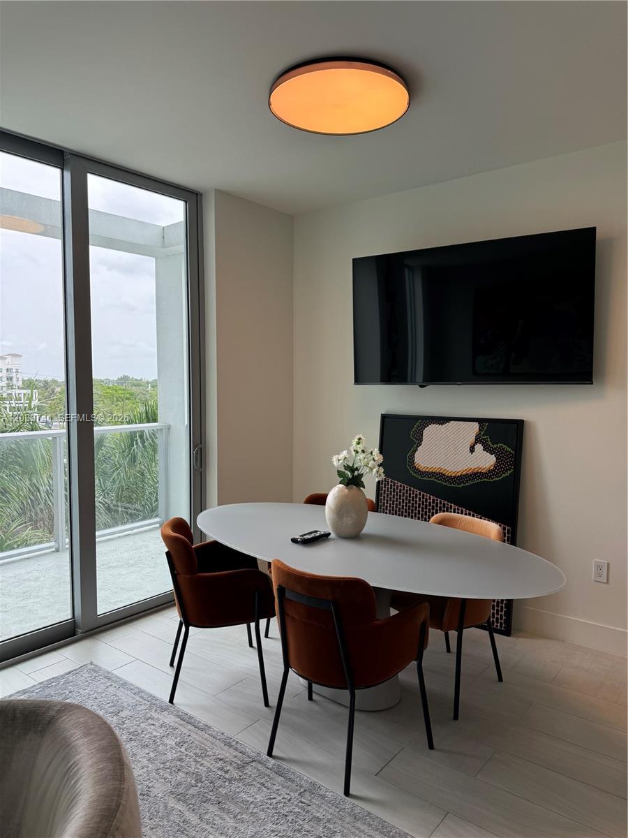 A dining area features an oval table, four orange chairs, a wall-mounted television, and balcony access — 2000 Metropica Way # 417, Sunrise FL 33323, SUNRISE, FL