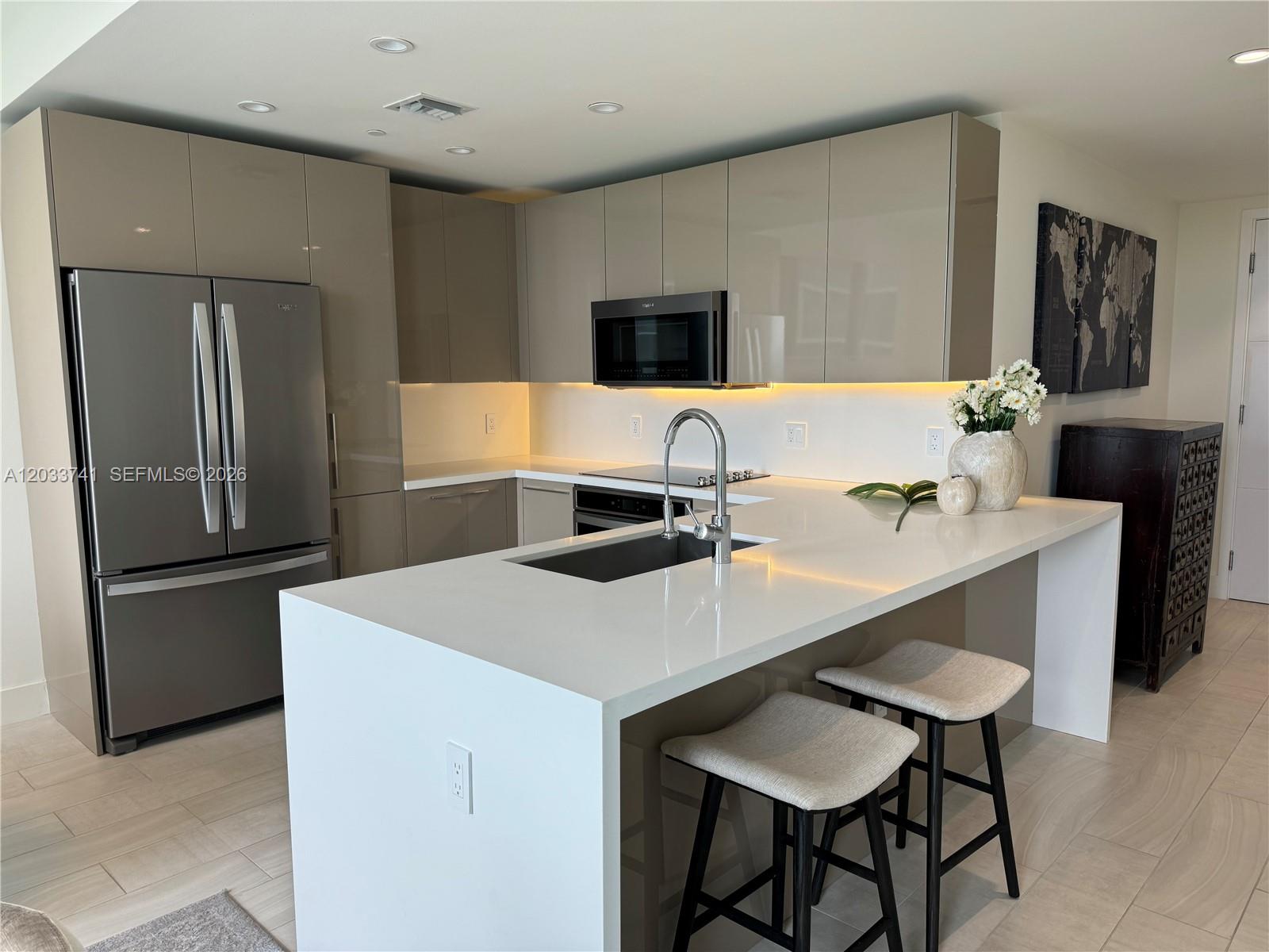A modern kitchen features glossy taupe cabinets, white quartz countertops, and a central island — 2000 Metropica Way # 417, Sunrise FL 33323, SUNRISE, FL